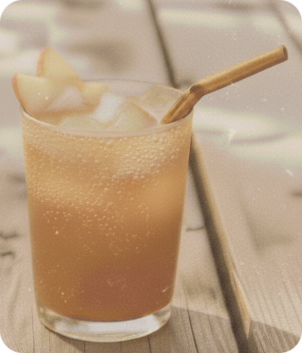 A refreshing glass of bubbly apple cider over ice, garnished with fresh apple slices and served with a wooden straw on a sunlit wooden table.