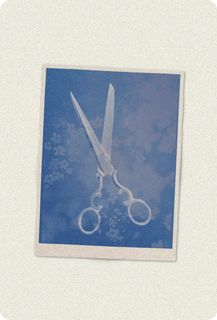 A cyanotype print of scissors with ornate handles, their white silhouette sharply outlined against a deep blue background with soft cloud-like patterns, styled like a vintage photograph on textured paper.