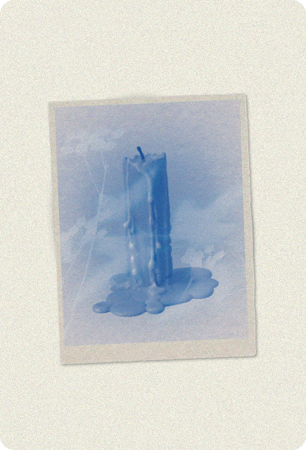 A cyanotype print of a tall candle with wax dripping down its sides and pooling at the base, shown as a soft white silhouette against a misty blue background, framed like a vintage photograph on textured paper.