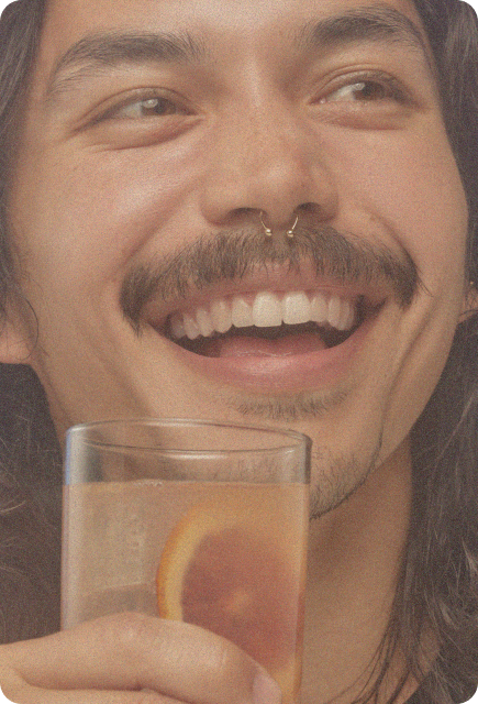Smiling person with a mustache holding a citrus-garnished drink in a clear glass.