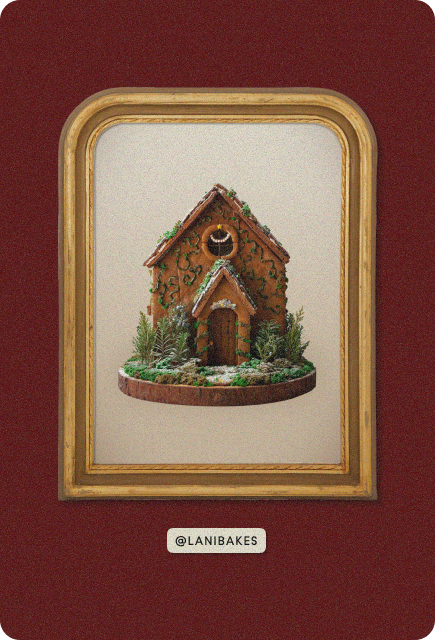 A whimsical moss-covered gingerbread cottage with sugar-coated trees and powdered-sugar snow, crafted by @lanibakes.