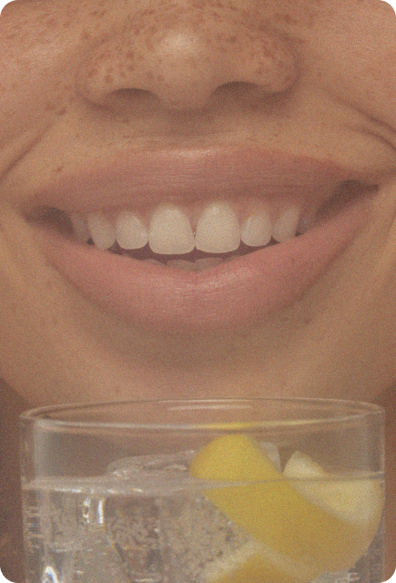 Close-up of a smiling person holding a glass with ice and a lemon peel garnish.