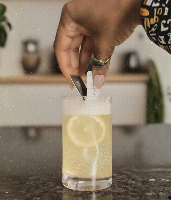 A hand squeezes a Wims Pocket-Tonic™ sachet into a glass of sparkling lemon drink, capturing the moment the THC/CBD blend mixes with citrus for a refreshing, elevated beverage experience.