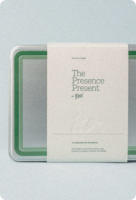 Wims “The Presence Present” holiday countdown calendar shown in a metal tin with green detailing and a minimalist cream wraparound label featuring the product name and description.