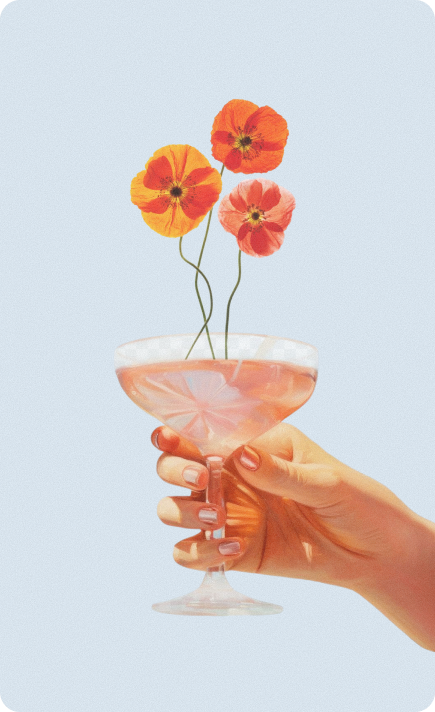 Hand holding a coupe glass filled with a light pink drink, garnished with three vibrant poppy flowers in shades of orange, yellow, and pink, against a pale blue background.