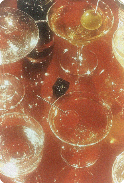 Sparkling cocktail glasses with olives and cherries on a glowing table, representing celebratory drinks and elevated hosting rituals.