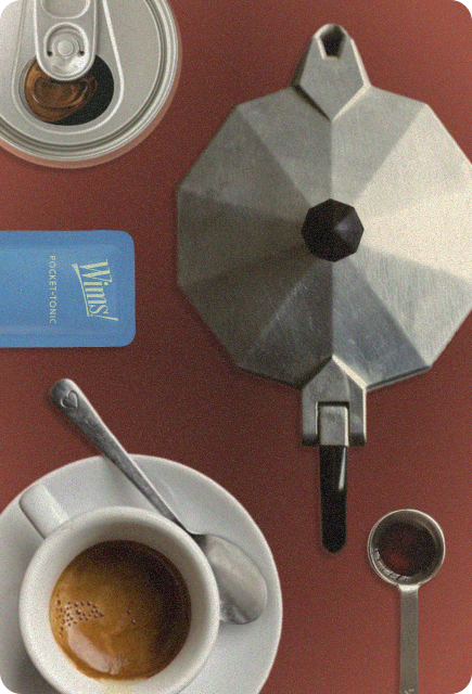 Overhead view of an espresso cup, moka pot, and Unflavored Wims Pocket-Tonic™ arranged on a warm red surface.