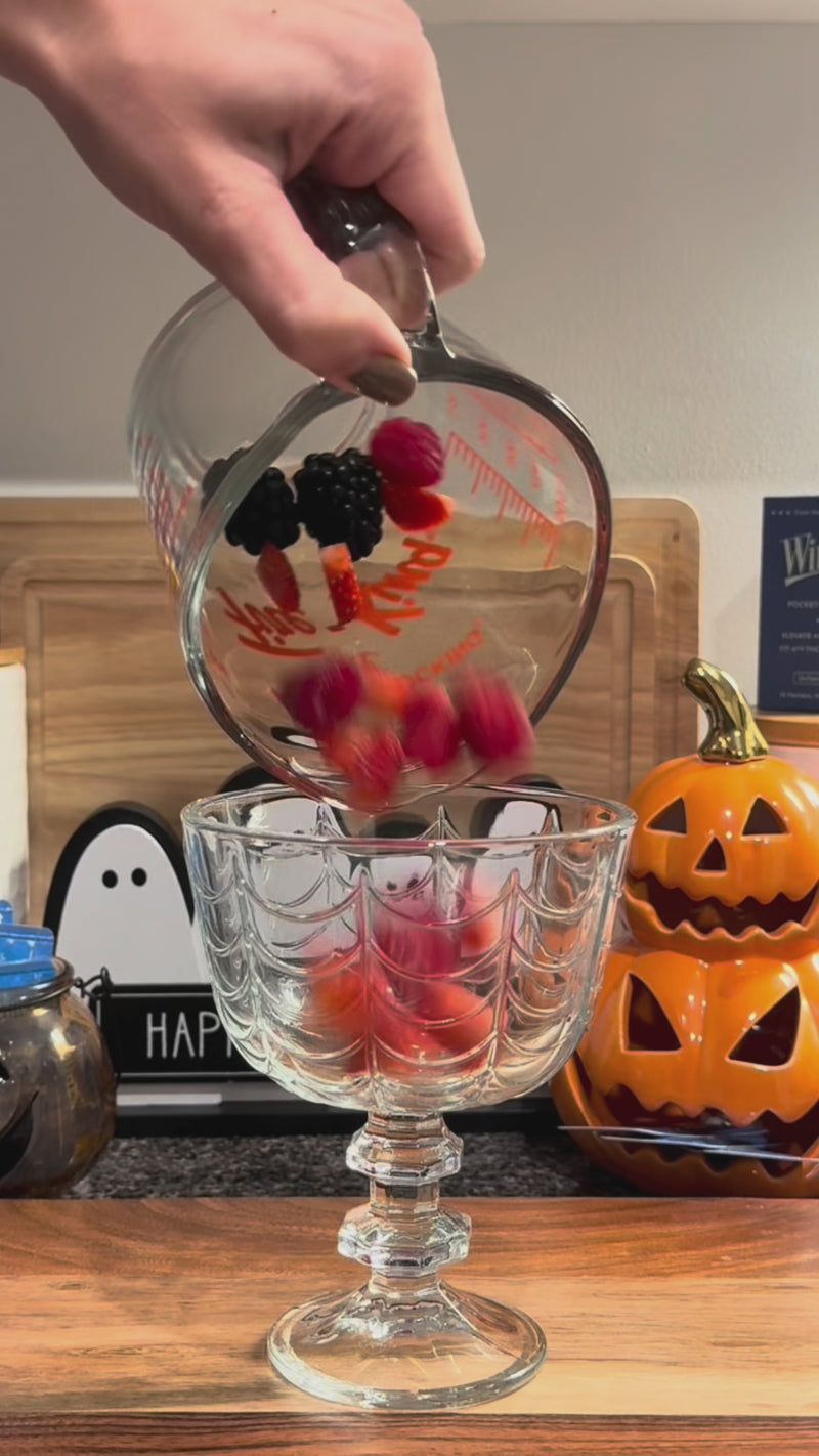 Fresh strawberries, raspberries, and blackberries being muddled with lemon juice in a glass to create the base of the Triple Berry Spritz.