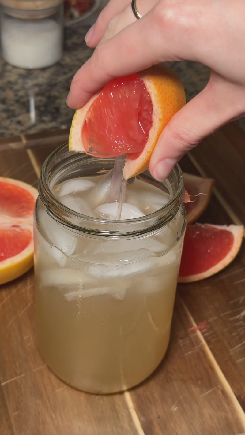 Fresh grapefruit juice being squeezed into the finished Citrus Grove Spritz before garnishing with a grapefruit wedge and serving.