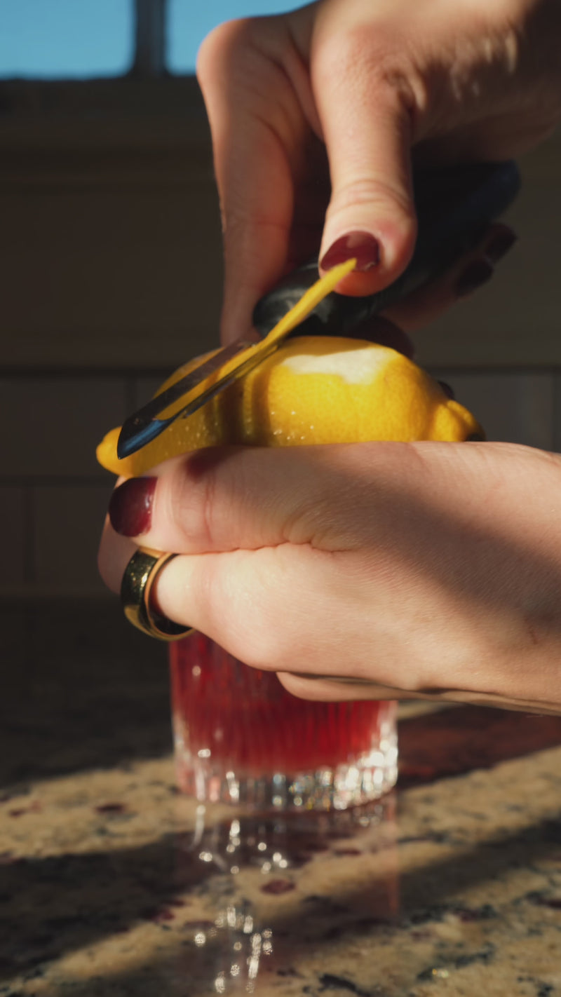 A fresh strip of lemon peel is cut from a whole lemon, twisted, then placed into the glass as the final garnish.