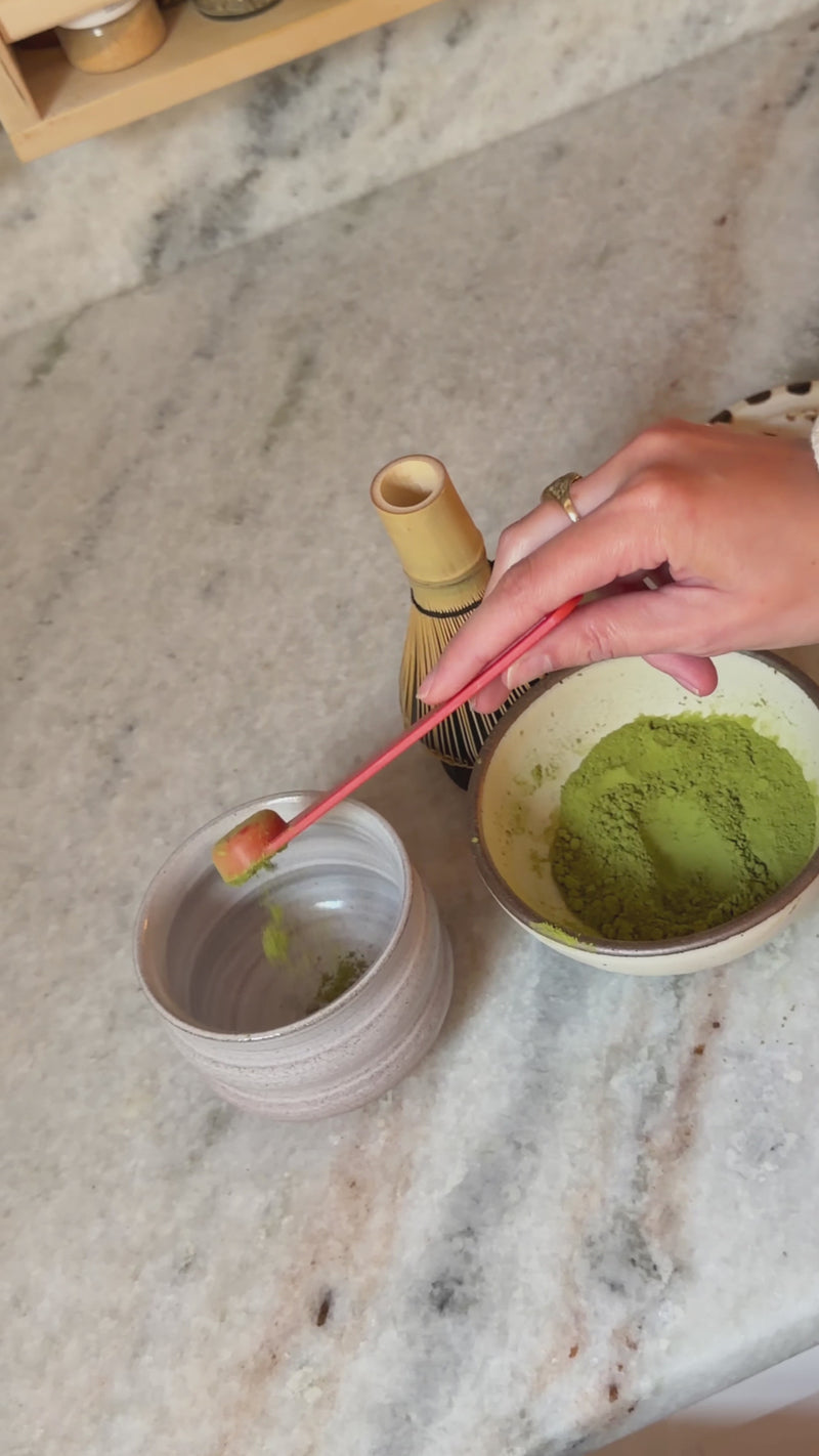 Matcha powder being whisked with hot water using a bamboo whisk in a small bowl until smooth and lightly frothy.