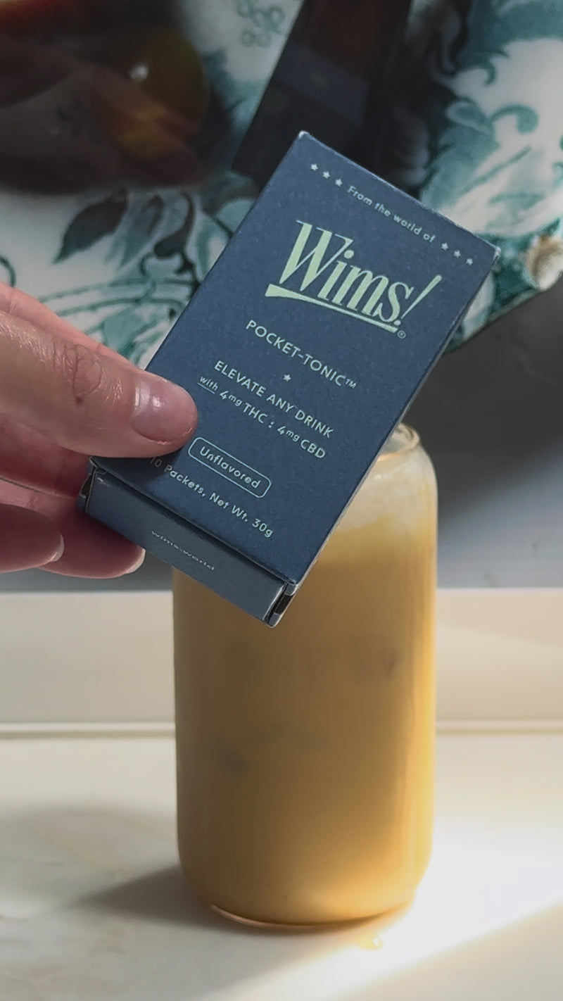  Wims Unflavored Pocket-Tonic™ being squeezed into the iced latte for a subtle herbal twist, followed by a sprinkle of cinnamon on top. The finished drink sits beside the Wims box and Cometeer capsule, ready to enjoy as a cozy fall THC/CBD latte.