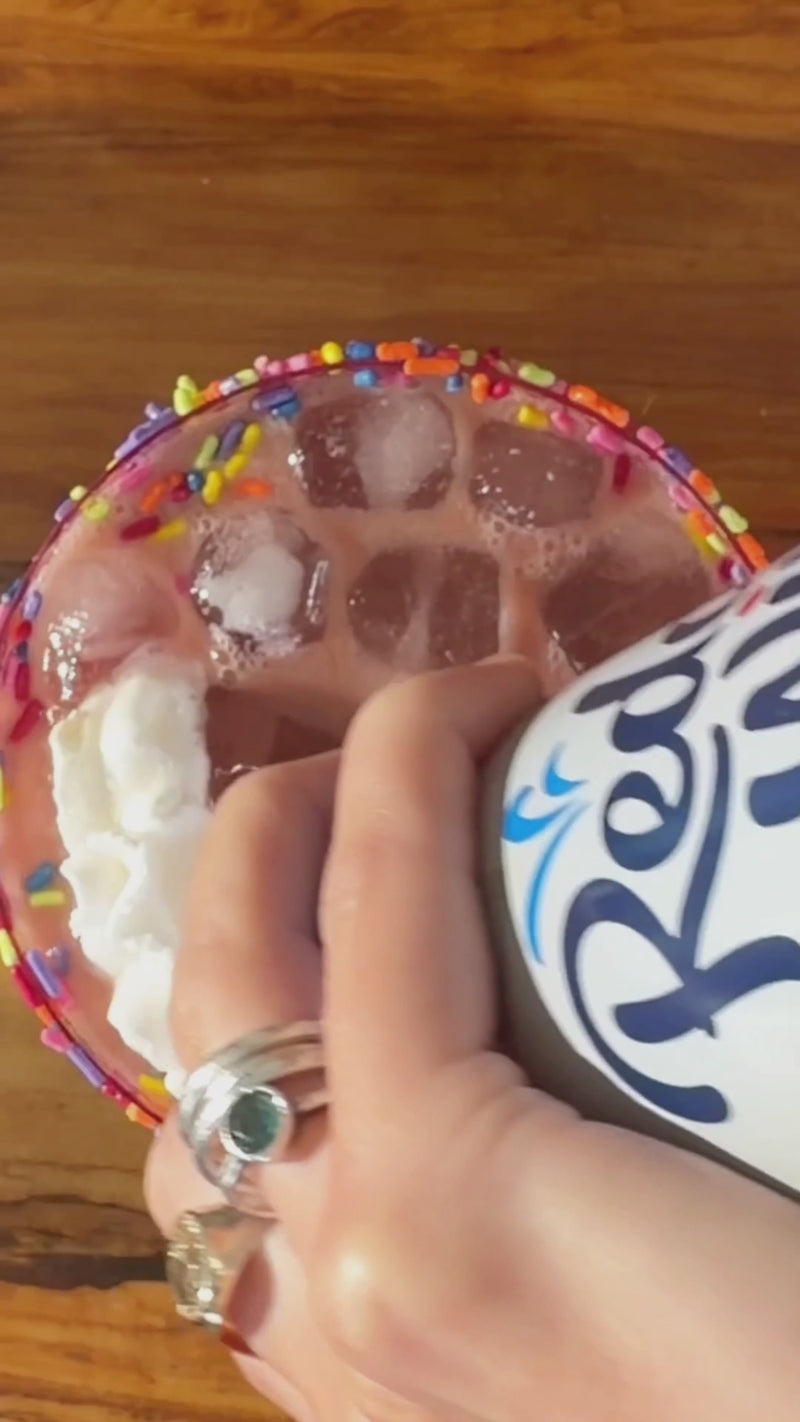 Whipped cream being added to the finished Pride Mocktail and topped with rainbow sprinkles, creating a festive, colorful finish ready to enjoy.