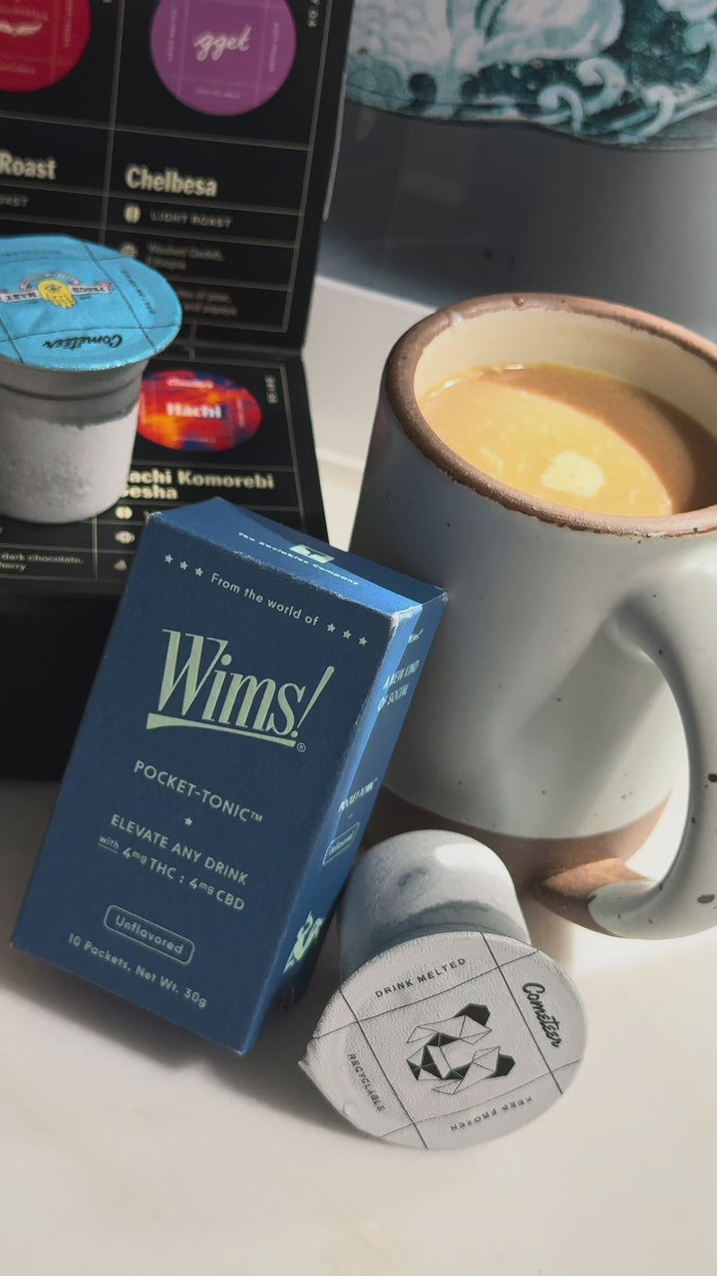 A steaming mug of hot latte sits on a cozy surface beside a Wims Unflavored Pocket-Tonic™ box and a Cometeer coffee capsule, ready to enjoy with a comforting finishing touch like cinnamon, cocoa powder, or honey.
