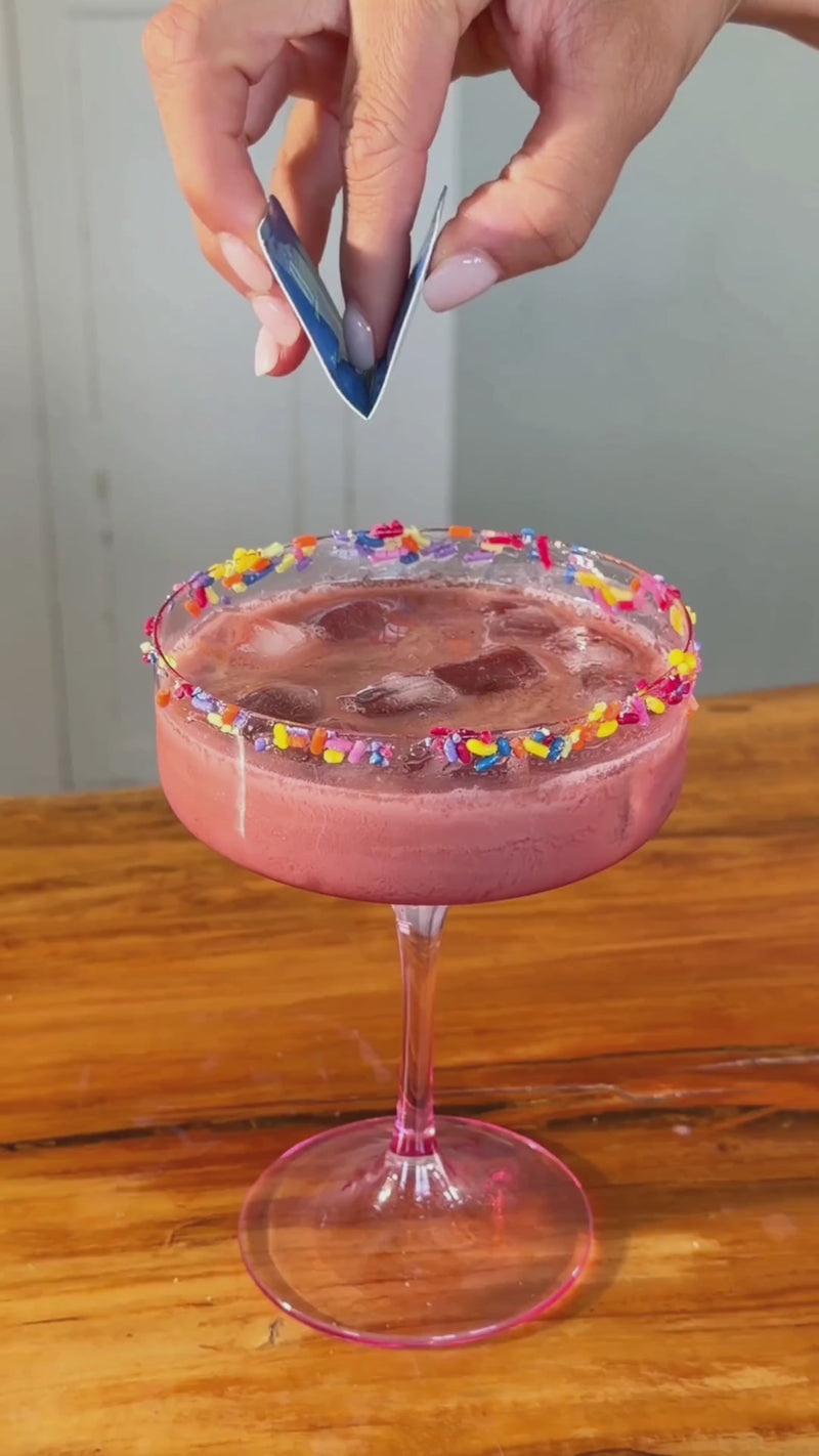 Unflavored Wims Pocket-Tonic™ being snapped open and added to a watermelon coconut mocktail with a rainbow sprinkle rim, ready to be stirred into the drink.