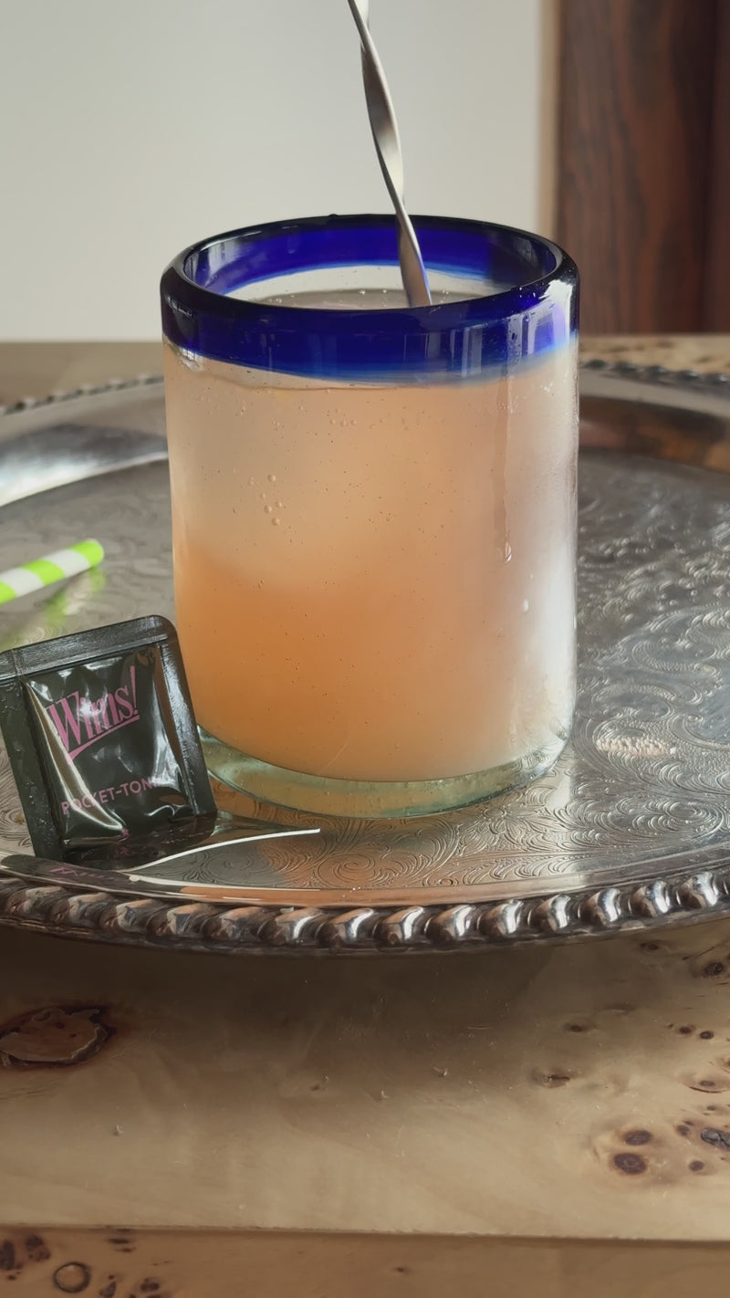 Hand squeezing a fresh orange slice over a glass topped with sparkling water, then lightly stirring the blood orange mocktail to combine before serving.