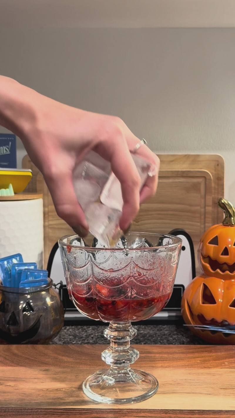 Cranberry juice and pomegranate juice being poured over ice and muddled berries to create a deep red Halloween mocktail.