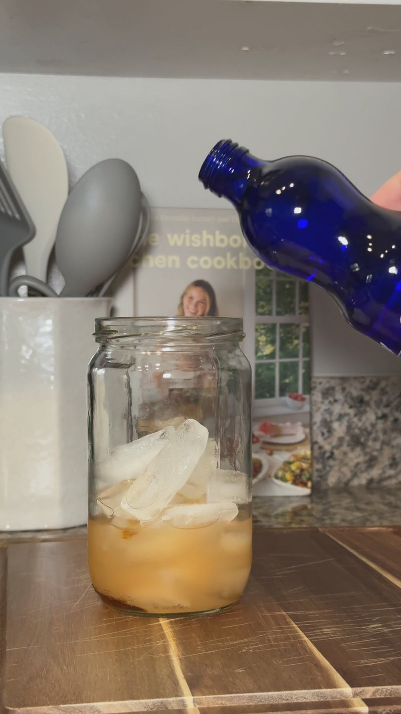 Sparkling soda water being poured into the grapefruit mixture over ice before gently stirring to combine.