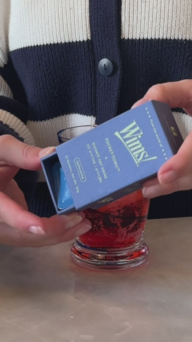 A short rocks glass with a vibrant cherry soda mixture is shown as an Unflavored Wims Pocket-Tonic™ is snapped open into the drink. A fresh lime wedge is placed on the rim as the final garnish.