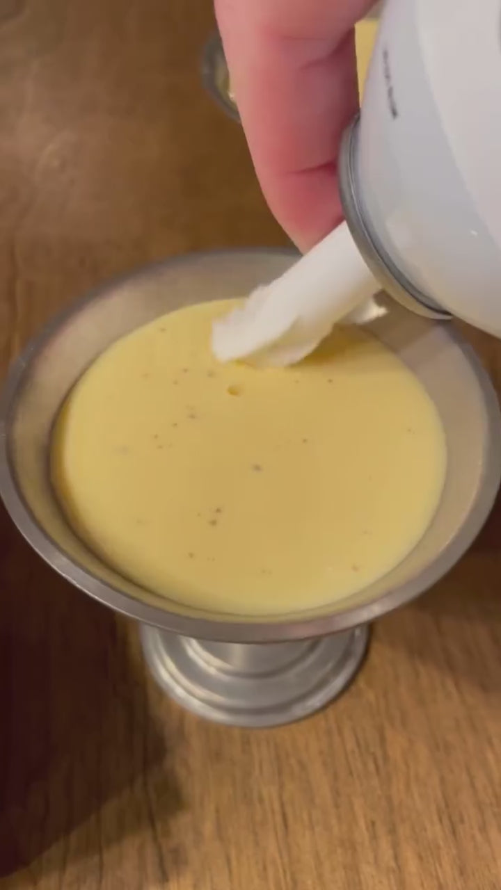 Festive egg nog shooters on a wooden table, each topped with a swirl of whipped cream and a dusting of nutmeg, looking like the perfect Christmas party treat.