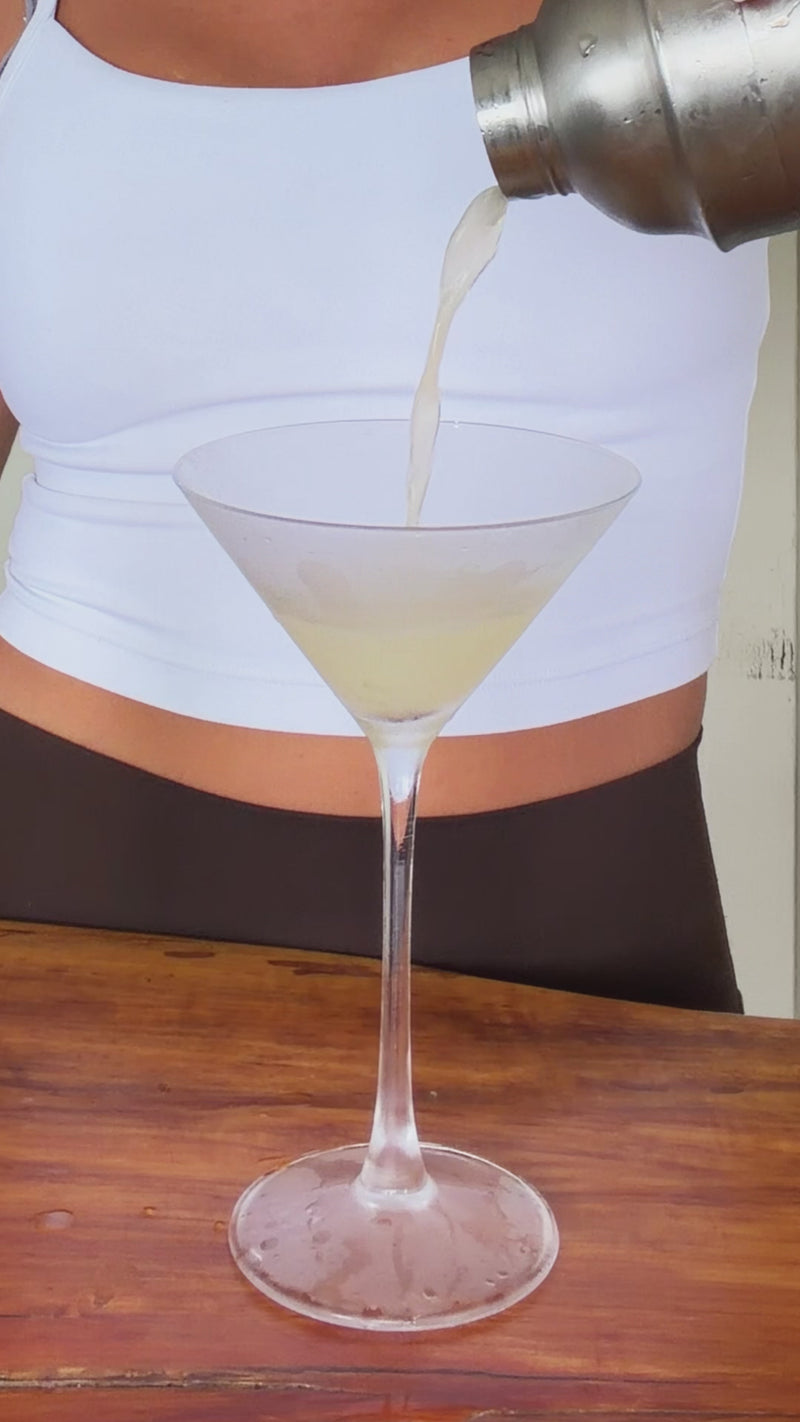 Pickletini being strained into a glass, topped with sparkling water, and garnished with a pickle slice.
