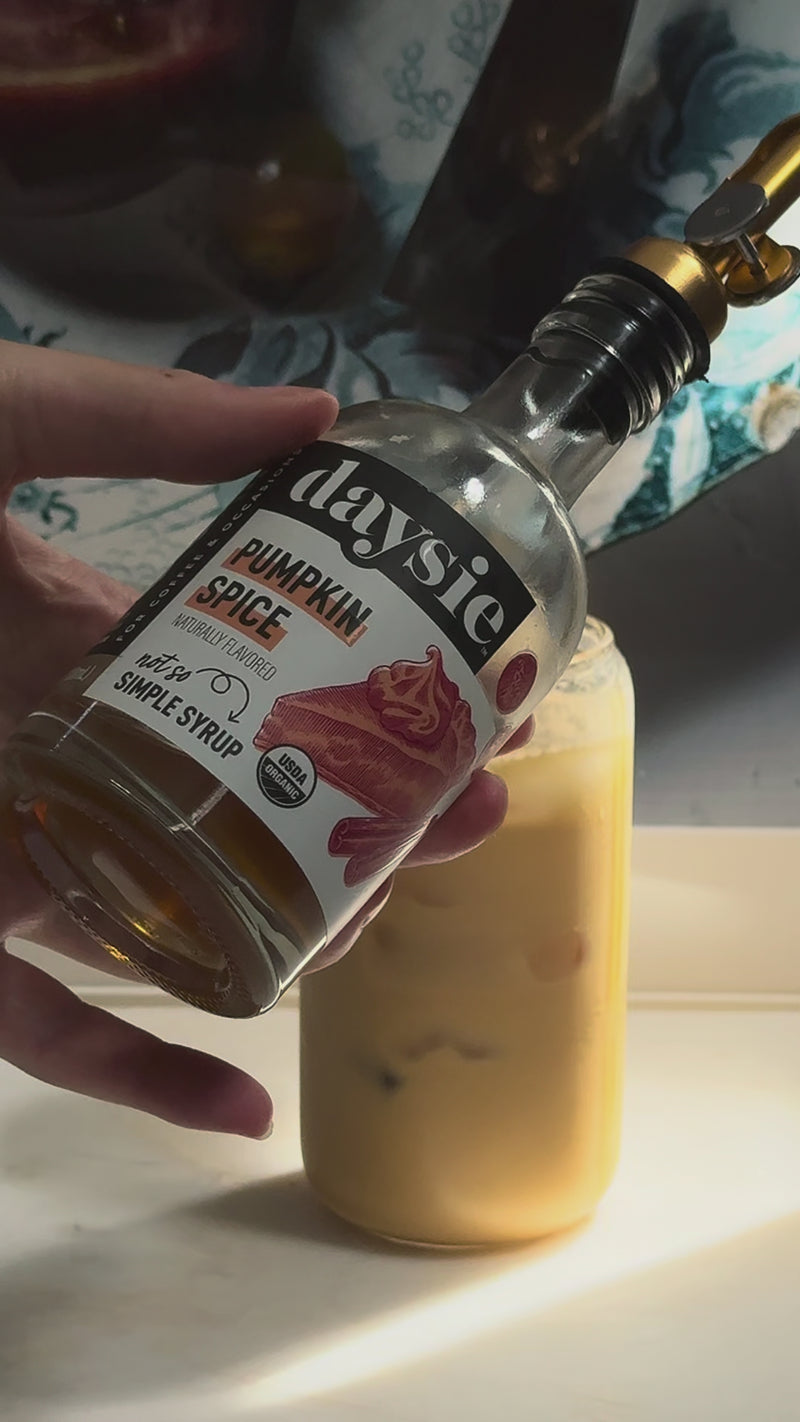 Pumpkin spice syrup being drizzled into a tall glass of iced latte, adding cozy fall flavor and sweetness.