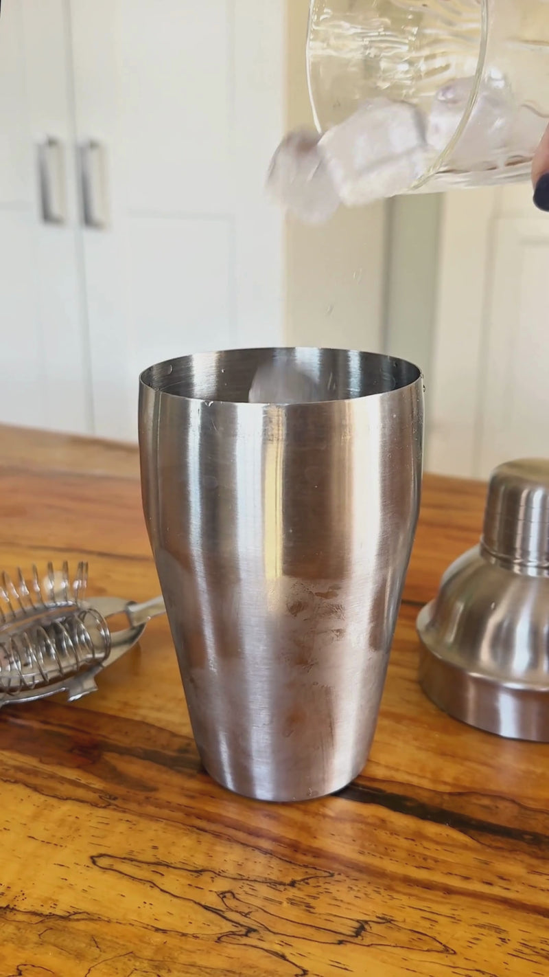 Ice added to a stainless steel cocktail shaker followed by non-alcoholic gin or vodka alternative, vermouth alternative, and olive brine for a Dirty Martini.