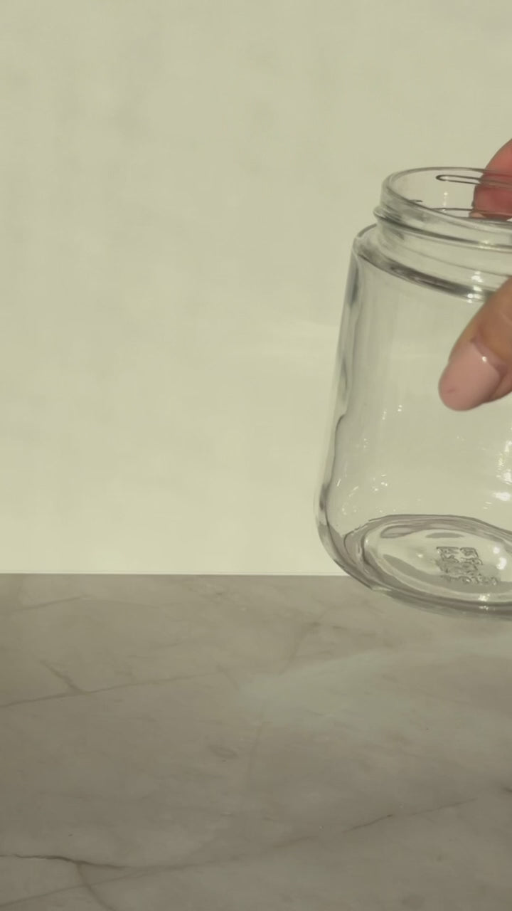 Pouring the warm cranberry syrup from a saucepan into a heat-safe glass jar, with the deep red liquid and softened cranberries transferring as it cools.