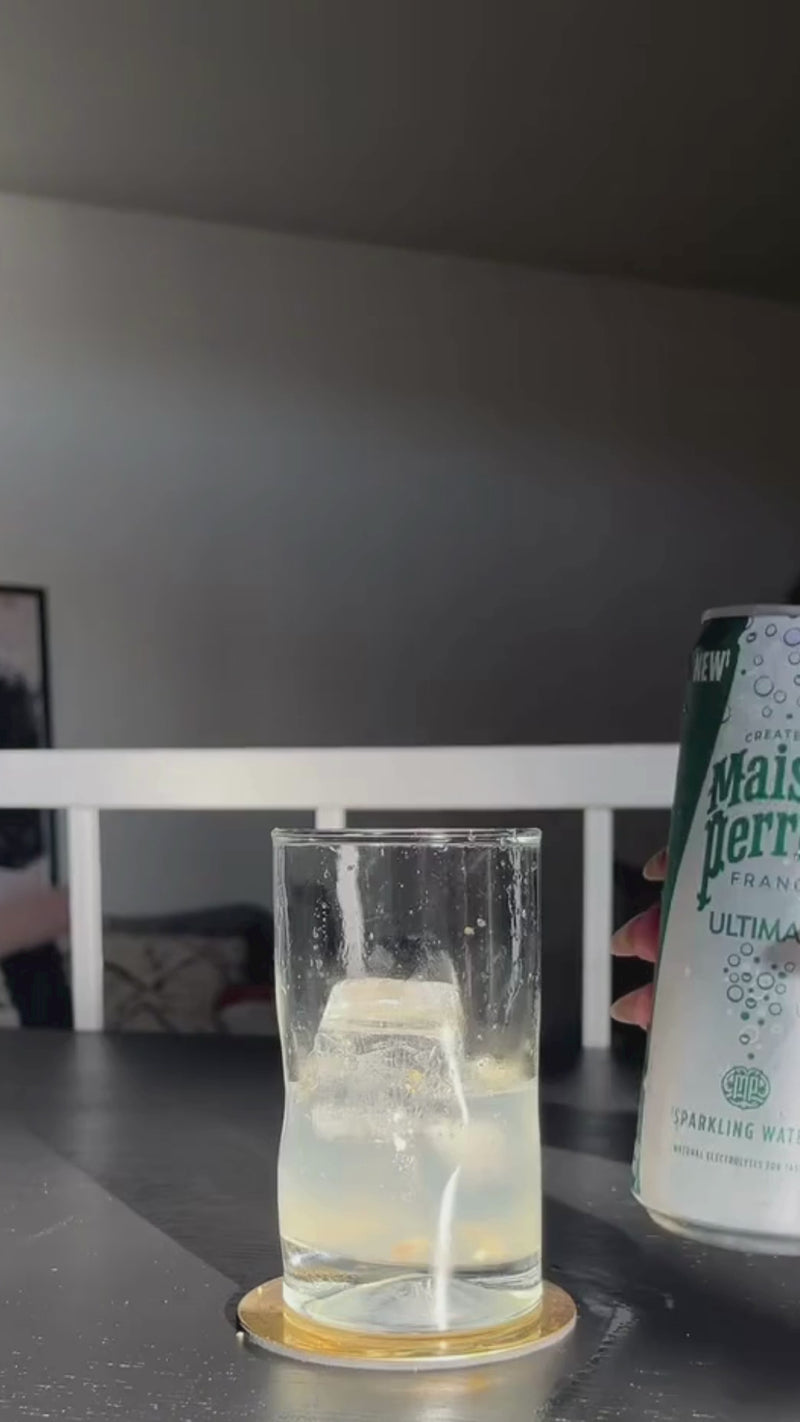 A hand pours sparkling water and ginger beer into the tall glass. The drink begins to fizz, creating a bubbly, refreshing base.