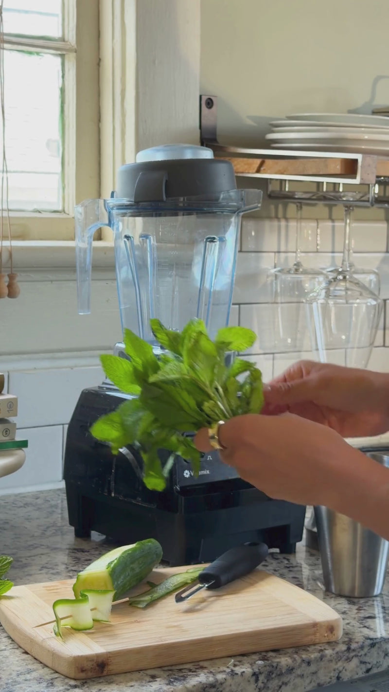 Fresh mint leaves and lime juice being muddled in a cocktail shaker to release bright, refreshing flavor for a Frozen Hugo Spritz.