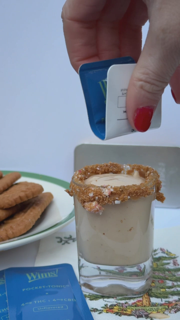 A Wims Unflavored Pocket-Tonic™ is poured into a cookie butter shot with a cookie-crumb-coated rim, sitting on a white surface with cookies and a blue Unflavored Wims Pocket-Tonic™ nearby.